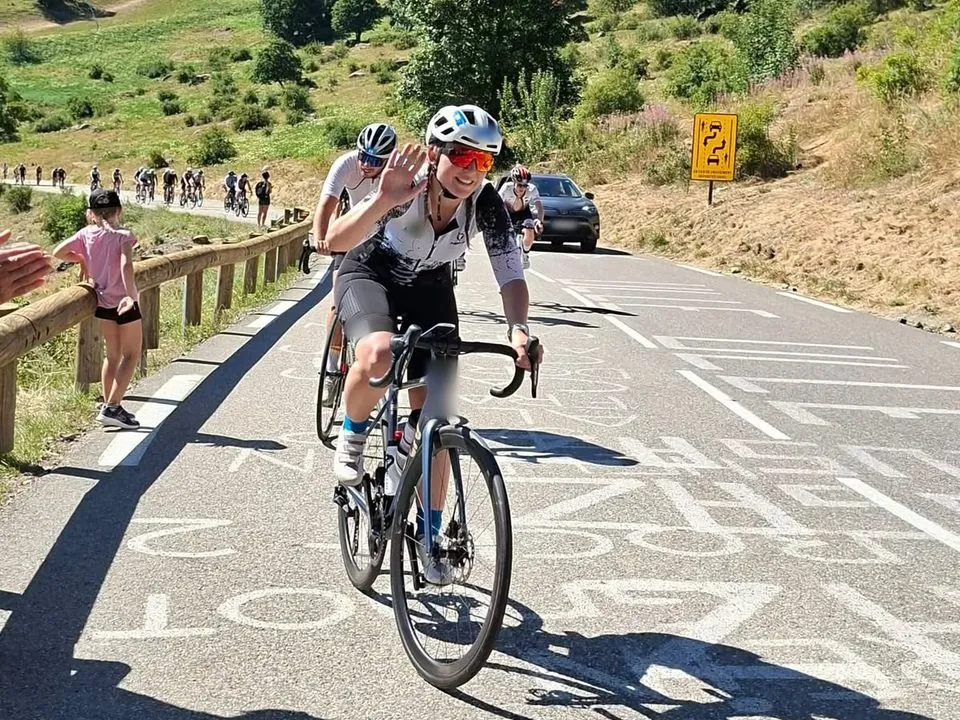 Jessica salue de la main pendant une montée à vélo en montagne